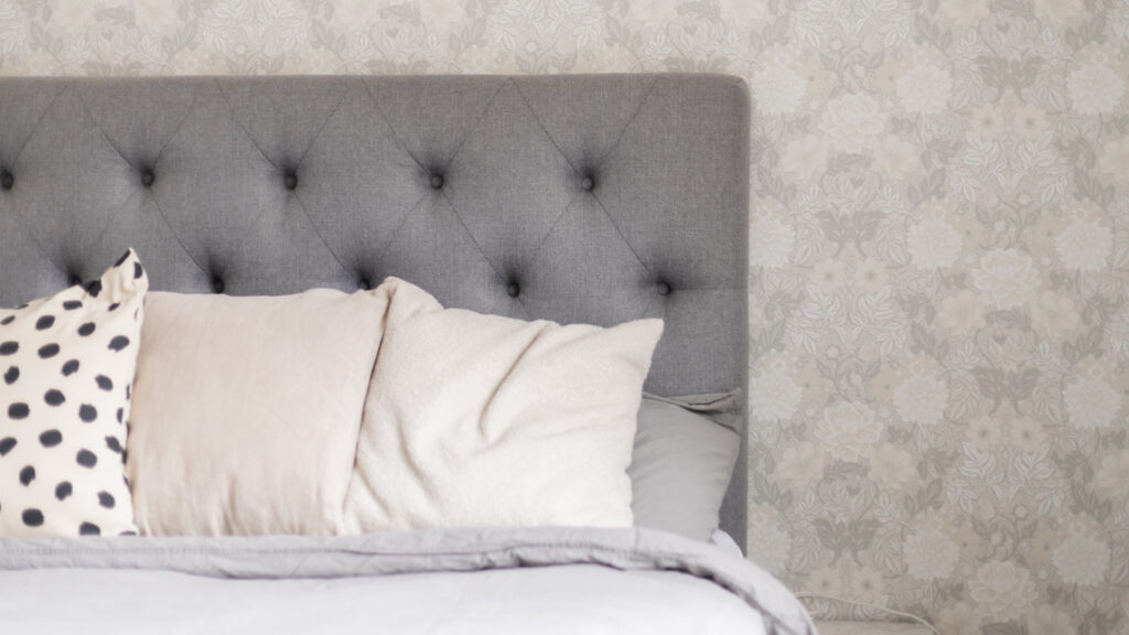 Grå sänggavel med kuddar framför.