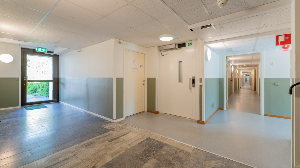 Entré i lägenhetshus med lång korridor.