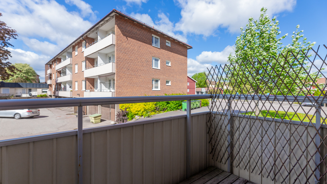 Från en balkong ser man ett flerfamiljshus och några träd.