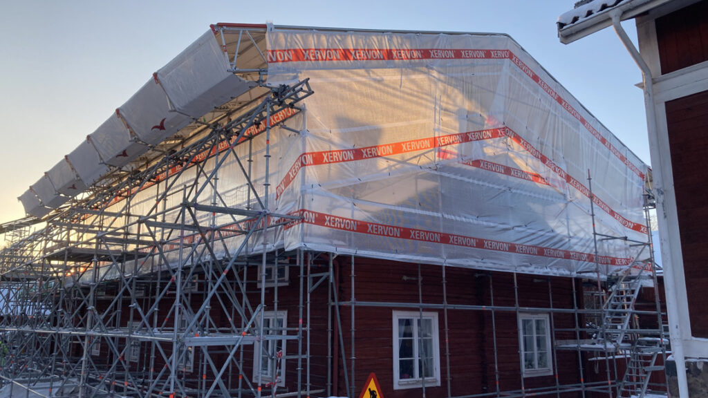 Byggställning med plast över ett bostadshus.