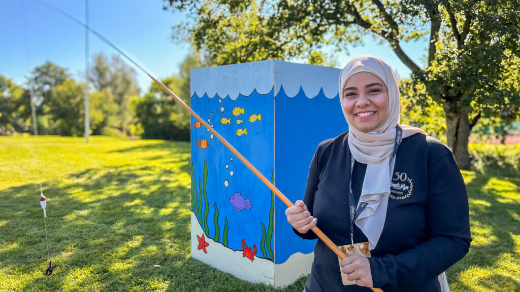 En glad kvinna håller i ett fiskespö framför en fiskedamm.
