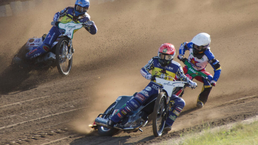 Tre speedwayförare på sina speedwaycyklar i full fart på banan.