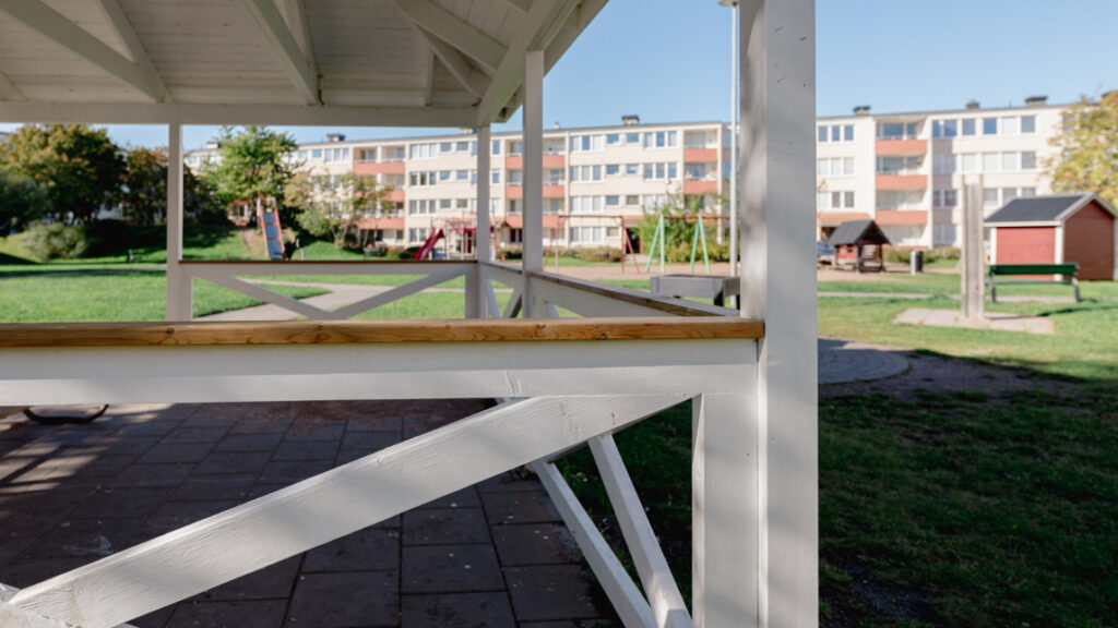 Vitmålad paviljong vid en lekpark.