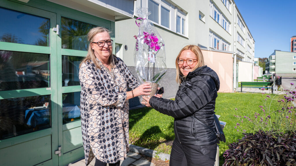 En kvinna räcker över en blomma till en annan kvinna.