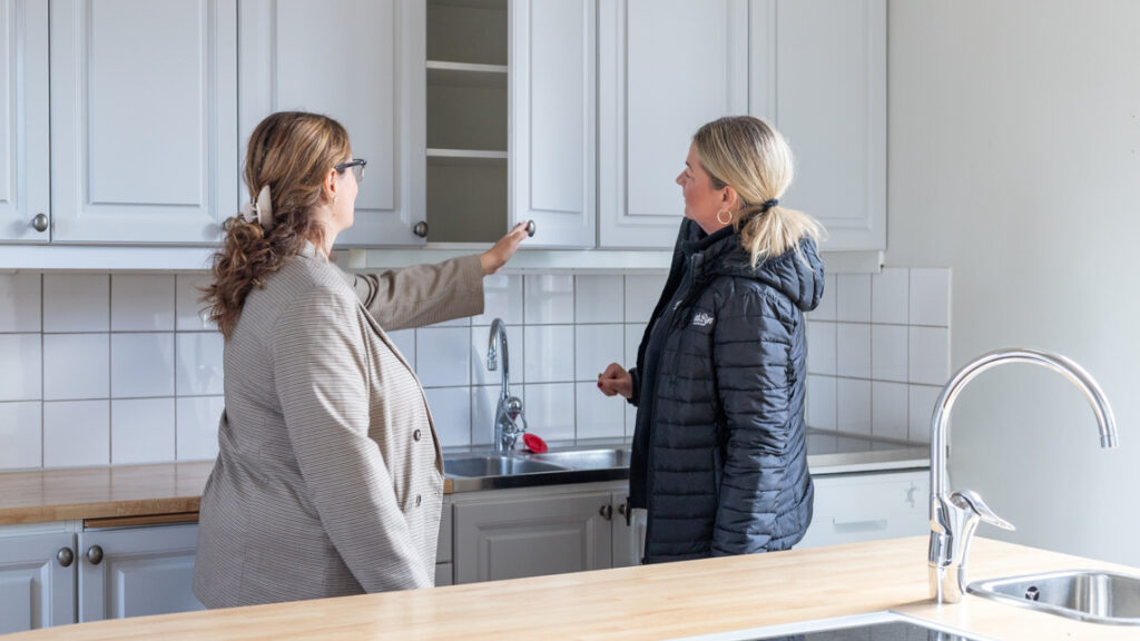 Två kvinnor står i ett kök och pratar.