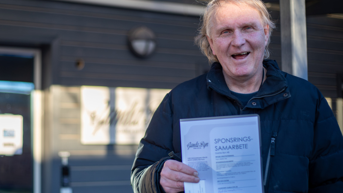 En glad man håller upp ett papper.