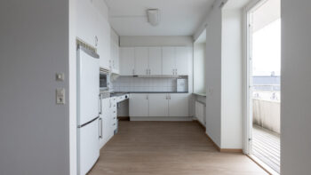 Ett tomt kök med vita skåp och trägolv.