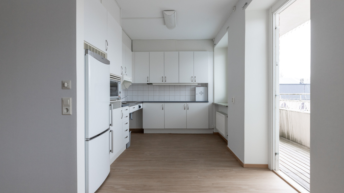 Ett tomt kök med vita skåp och trägolv.