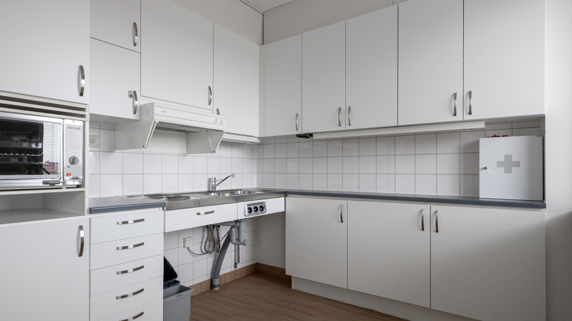 Ett tomt kök med vita skåp och trägolv.