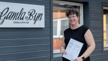 En kvinna står framför en byggnad och håller i ett papper.