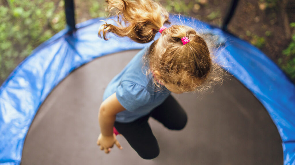 En flicka hoppar i en studsmatta i solsken.