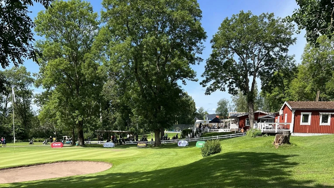 Två rödmålade hus i en vacker golfmiljö.